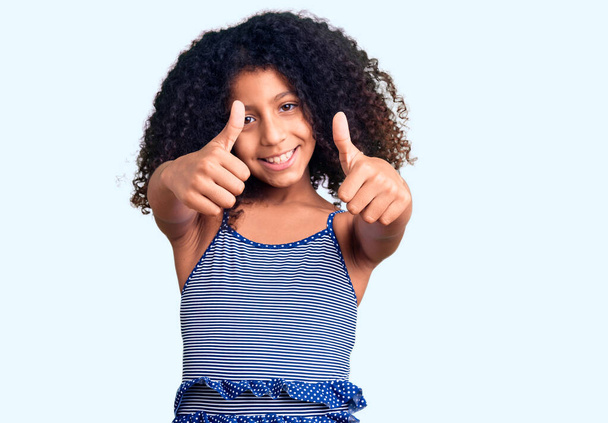 Африканське американське дитя з кучерявим волоссям у плавальному костюмі, яке схвалює позитивний жест рукою, підносить великий палець, посміхається і щасливий за успіх. жест переможця.  - Фото, зображення