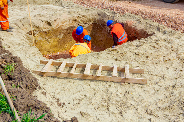 Arbeiter setzen Schaufeln ein, um in einem quadratischen Graben ein ebenes Fundament zu errichten.. - Foto, Bild