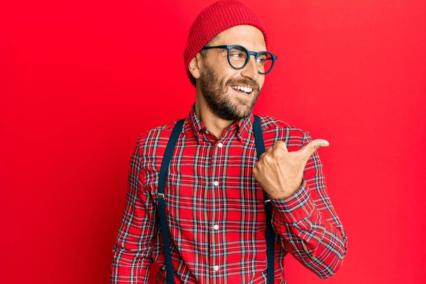 Красивый мужчина с бородой в хипстерской элегантный вид указывая большой палец вверх в сторону улыбается счастливо с открытым ртом  - Фото, изображение