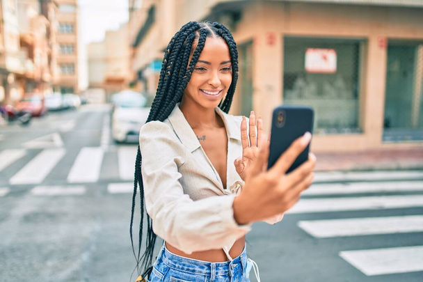 Mladý africký Američan žena usměvavý šťastný dělat videohovor pomocí smartphone ve městě. - Fotografie, Obrázek
