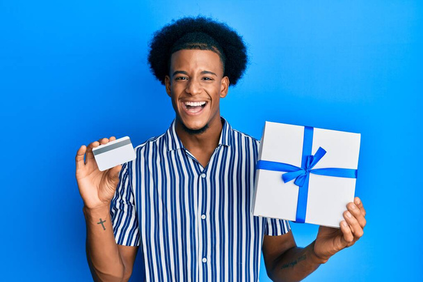 Африканський американець з африканським волоссям, який тримає подарунок і кредитну картку посміхається і сміється голосно, тому що смішний жарт.  - Фото, зображення