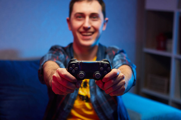 Portret szalonego, zabawnego gracza, chłopca cieszącego się graniem w gry wideo w pomieszczeniach, siedzącego na sofie, trzymającego w rękach Gamepad konsoli. Odpoczywaj w domu, miłego weekendu. - Zdjęcie, obraz