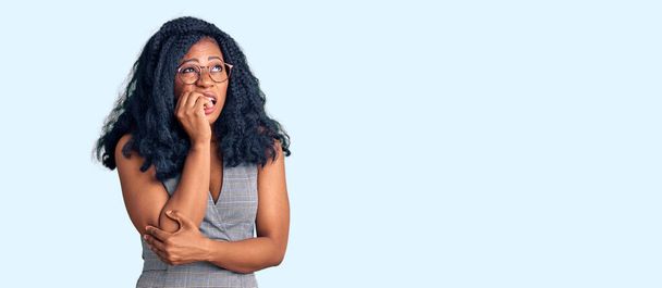 Schöne afrikanisch-amerikanische Frau in Businesskleidung und Brille sieht gestresst und nervös aus, die Hände auf den Mund beißenden Nägeln. Angstproblem.  - Foto, Bild