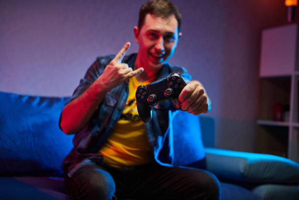 Portrait of crazy playful Gamer, boy enjoying Playing Video Games indoors sitting on the sofa, holding Console Gamepad in hands. Resting At Home, have a great Weekend - Photo, Image