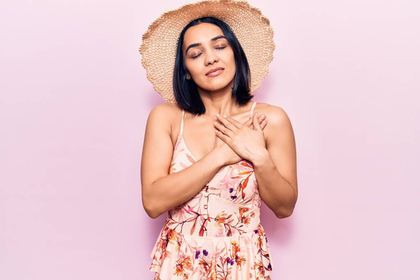 Young beautiful latin woman wearing summer hat smiling with hands on chest, eyes closed with grateful gesture on face. health concept.  - Fotoğraf, Görsel