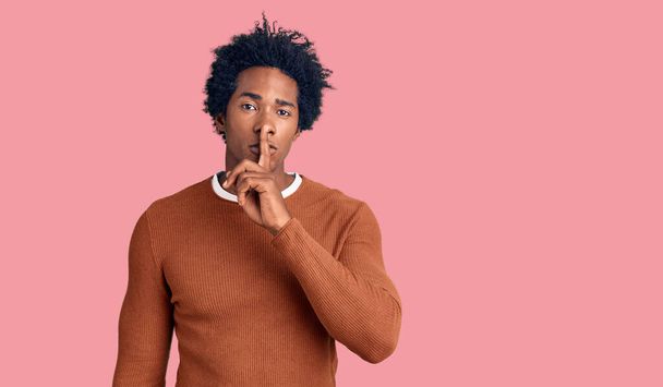 Hombre afroamericano guapo con el pelo afro usando ropa casual pidiendo estar tranquilo con el dedo en los labios. silencio y concepto secreto.  - Foto, imagen