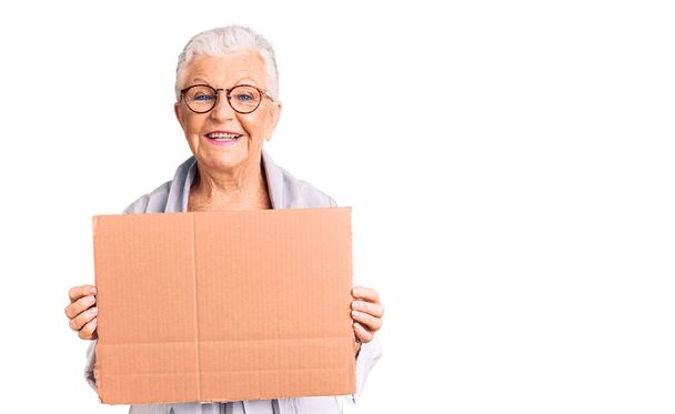 Senior schöne Frau mit blauen Augen und grauen Haaren halten wir brauchen einen Wechsel Banner sieht positiv und glücklich stehend und lächelnd mit einem selbstbewussten Lächeln Zähne zeigt  - Foto, Bild