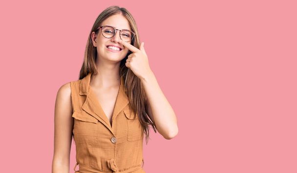 Young beautiful blonde woman wearing casual clothes and glasses pointing with hand finger to face and nose, smiling cheerful. beauty concept  - Fotoğraf, Görsel