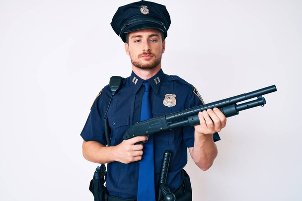 Polis üniforması giyen genç beyaz adam elinde pompalı tüfekle yüzünde ciddi bir ifadeyle rahatladı. Basit ve doğal bir şekilde kameraya bakıyorsun..  - Fotoğraf, Görsel