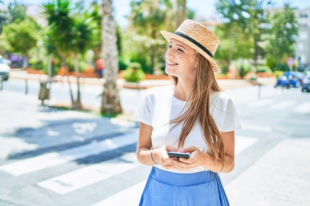 Mujer rubia joven de vacaciones sonriendo feliz usando el teléfono inteligente en la calle de la ciudad - Foto, imagen