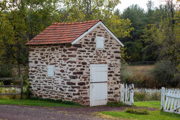 Maison de printemps en pierre coloniale avec volets en bois par porte de jardin blanche. - Photo, image