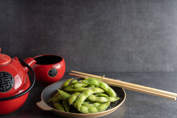 Japonský předkrm Edamame zelené sójové boby ochucené solí v misce, s prodejními tyčinkami na boku. - Fotografie, Obrázek