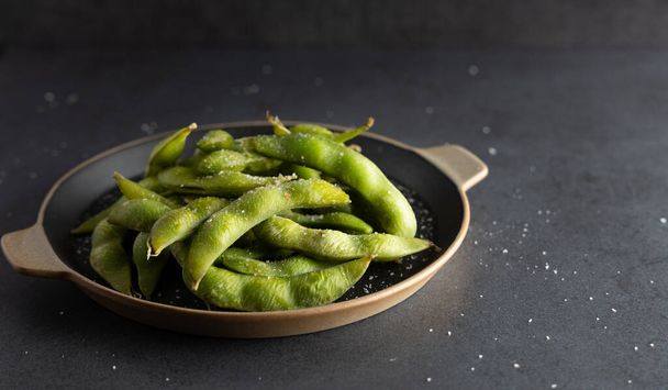 Japanese appetizer Edamame green soy beans seasoned with salt in a bowl, with shop sticks on the side. - Photo, Image