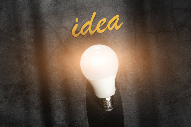 Лампочка на темном фоне и надпись "Идея". Концепция творчества. - Фото, изображение