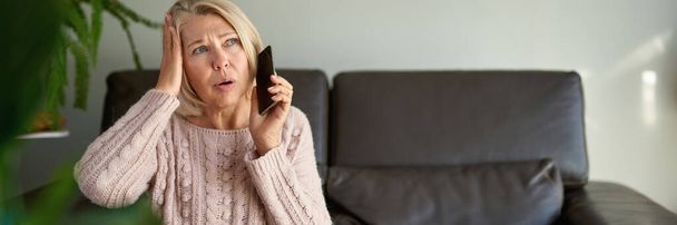 зріла жінка в телефонному дзвінку сидить на дивані у вітальні в будинку
 - Фото, зображення