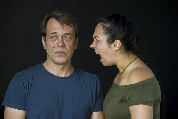 A woman yells at a man on a dark neutral background.The concept:family quarrel, conflict between people, suspicion of infidelity, lack of understanding, difficult period. - Foto, Imagen