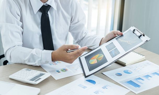 Az üzletember leül az asztalukhoz, és kiszámítja a pénzügyi grafikonokat, amelyek bemutatják a sikeres üzleti növekedés folyamatát tervező befektetéseik eredményeit.. - Fotó, kép