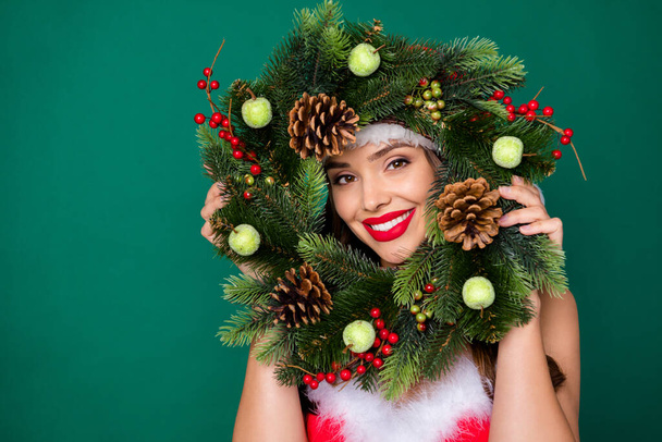 Photo of attractive lady look through newyear season circle wreath christmas tree door house entrance decor tradition good mood wear x-mas snow girl costume isolated green color background - Foto, immagini
