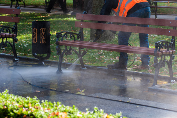wysokociśnieniowy strumień wody, pracownik myje ulice wodą z pistoletu wodnego, czyste ławki w parku karher - Zdjęcie, obraz