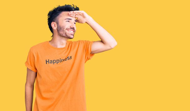 Mladý hispánec v tričku se šťastným slovem, velmi šťastný a usmívající se s rukou nad hlavou. vyhledávací koncept.  - Fotografie, Obrázek