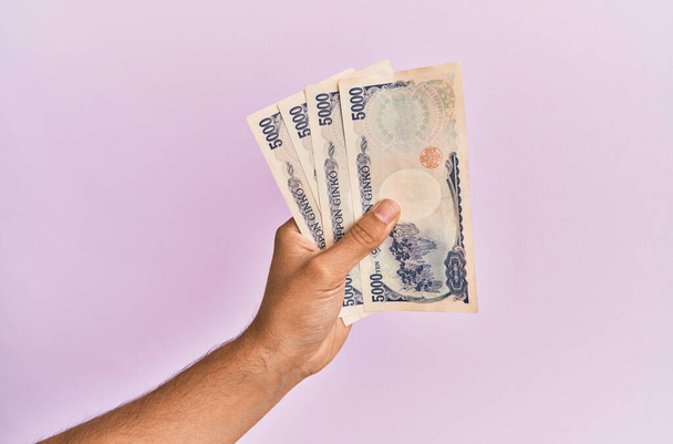 Latino käsi tilalla 5000 Japanin jeniä seteleitä yli eristetty vaaleanpunainen tausta. - Valokuva, kuva