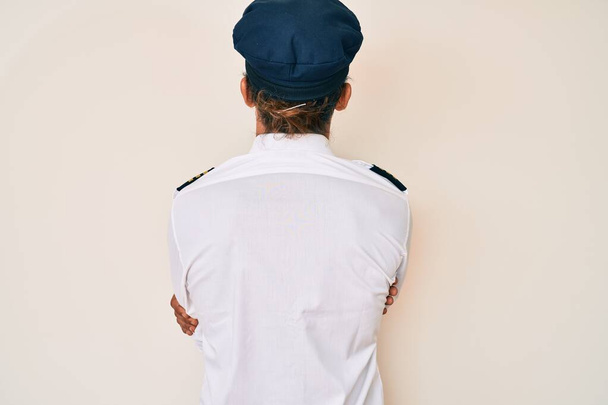 Uçak pilotu üniforması giyen İspanyol genç adam arkasını dönüp çapraz kollarla diğer tarafa bakıyor.  - Fotoğraf, Görsel