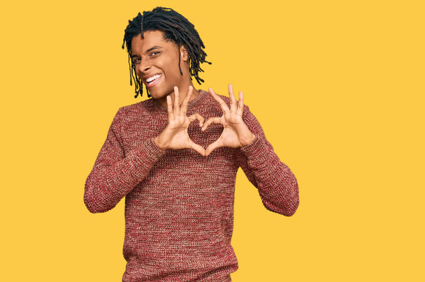 Mladý africký Američan nosí ležérní zimní svetr, usmívá se v lásce a ukazuje symbol srdce a tvar rukama. romantický koncept.  - Fotografie, Obrázek