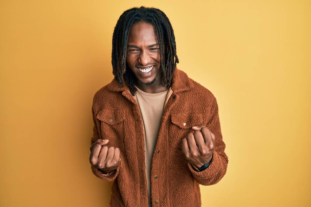 Homme afro-américain avec des tresses veste rétro marron célébrant surpris et étonnés pour le succès avec les bras levés et les yeux fermés. concept gagnant.  - Photo, image
