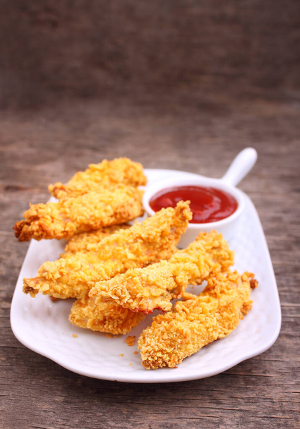 Delicious crispy fried chicken breast strips on white plate, on old rustic wooden table with tomato sauce  - Photo, Image