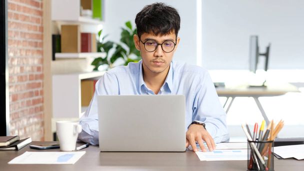 Młody azjatycki biznesmen koncentruje się na pracy z laptopem w biurze, azjatycki biurowiec kontemplować na laptopie, Azji męskich ludzi biznesu i koncepcji stylu życia biurowego - Zdjęcie, obraz