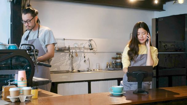 Fiatal ázsiai barista rendezés mobiltelefon és digitális tabletta a pultnál kávézó, ázsiai kisvállalkozás tulajdonosa, start up - Fotó, kép