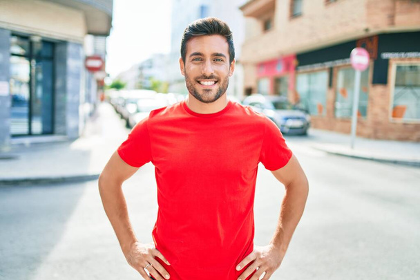 A fiatal jóképű spanyol férfi boldogan mosolyog. Mosollyal az arcán állni a város utcáján.. - Fotó, kép
