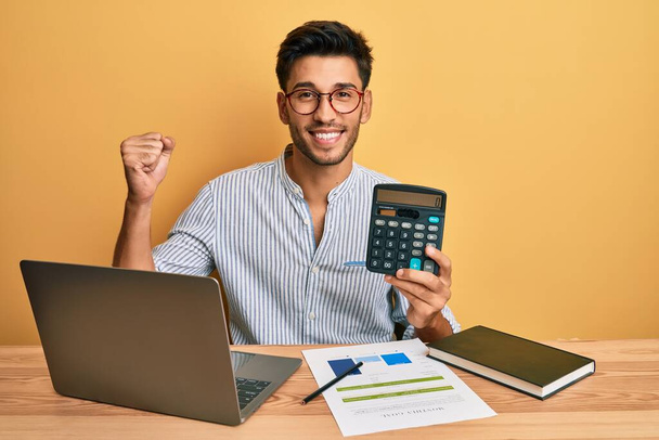 Mladý pohledný muž ukazující kalkulačku v kanceláři  - Fotografie, Obrázek