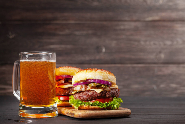 Dwa domowe smaczne hamburgery z dużą wołowiną, serem, pomidorem, bekonem, sałatą i kubkiem piwa. Z przestrzenią do kopiowania - Zdjęcie, obraz