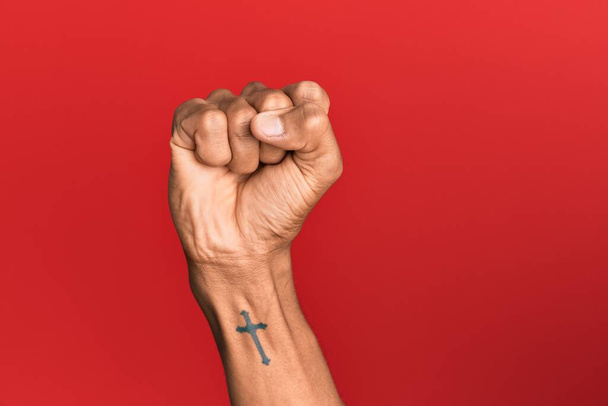 Hand van de Latijns-Amerikaanse man over rood geïsoleerde achtergrond doen protest en revolutie gebaar, vuist uiten kracht en macht  - Foto, afbeelding