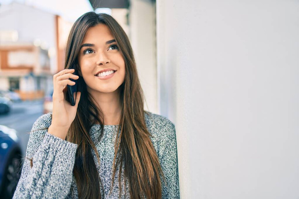 Fiatal gyönyörű spanyol lány mosolyog boldog beszél az okostelefonon a városban. - Fotó, kép