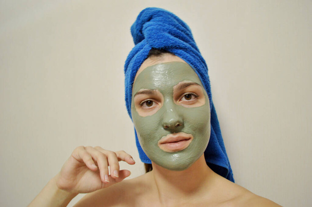 Frau mit blauem Handtuch auf dem Kopf und Tonmaske im Gesicht - Foto, Bild