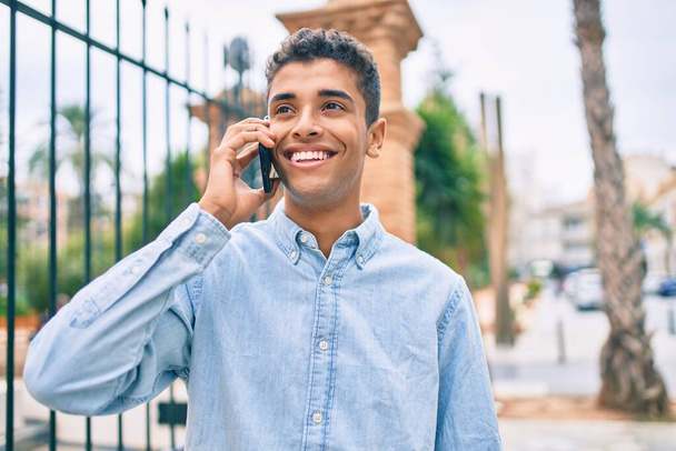 若いラテン語の男笑顔幸せな話上のスマートフォンで街を歩く. - 写真・画像