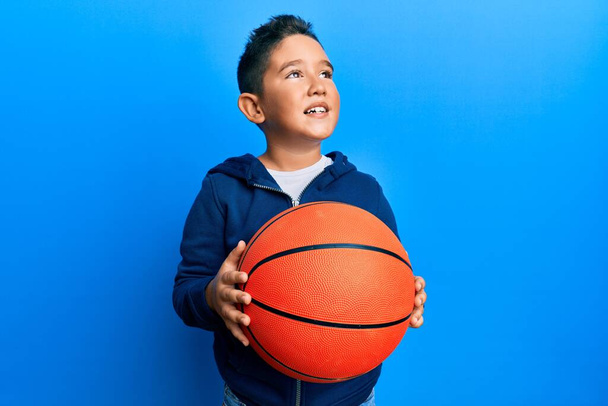 小さな男の子のヒスパニック系の子供バスケットボールボールを保持横に見て笑って離れて考えて見つめて.  - 写真・画像