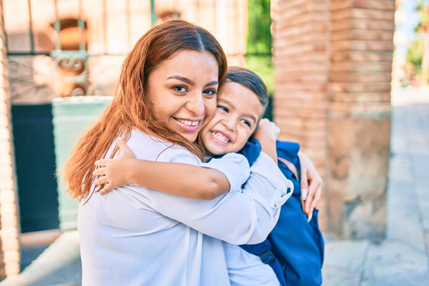 Adorable latin student boy and mom hugging at the city. - 写真・画像