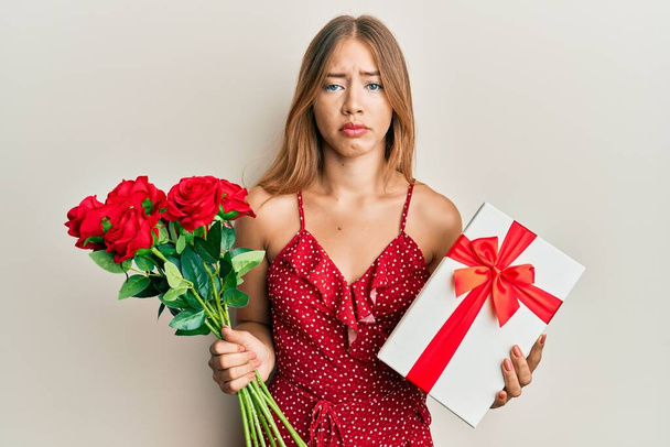 Beautiful young blonde woman holding anniversary present and bouquet of flowers depressed and worry for distress, crying angry and afraid. sad expression.  - Fotoğraf, Görsel