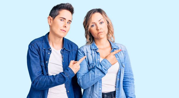 Couple de femmes portant des vêtements décontractés pointant avec le doigt de la main sur le côté montrant la publicité, visage sérieux et calme  - Photo, image