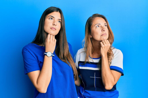 Hispanic family of mother and daughter wearing casual clothes over blue background with hand on chin thinking about question, pensive expression. smiling with thoughtful face. doubt concept.  - Photo, Image