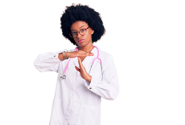 Giovane donna afroamericana vestita da medico cappotto e stetoscopio fare il gesto del tempo con le mani, viso frustrato e serio  - Foto, immagini