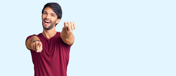 Knappe Spaanse man in casual kleding wijzend naar jou en de camera met vingers, lachend positief en vrolijk  - Foto, afbeelding