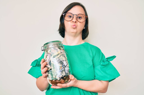 Brunette woman with down syndrome holding jar with savings looking at the camera blowing a kiss being lovely and sexy. love expression.  - Photo, Image