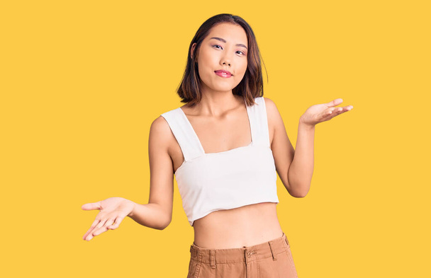 Young beautiful chinese girl wearing casual clothes clueless and confused expression with arms and hands raised. doubt concept.  - Photo, Image