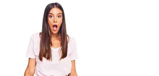 Jonge Latijns-Amerikaanse vrouw draagt casual wit tshirt bang en geschokt met verrassing en verbaasde uitdrukking, angst en opgewonden gezicht.  - Foto, afbeelding