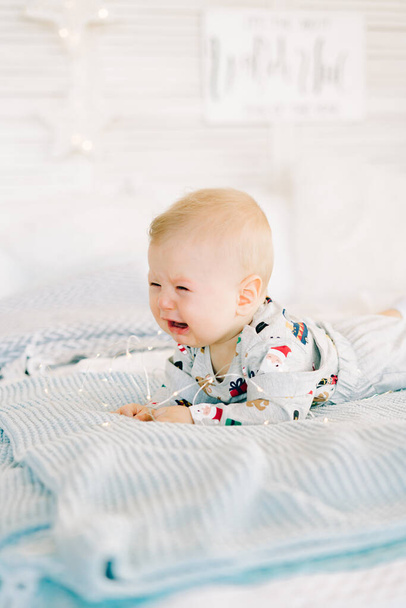 the child's first Christmas. sad, crying,a little boy is lying in a festive costume on the bed in a bright room.Christmas concept. - Фото, изображение