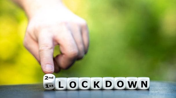 Symbool voor een tweede afsluiting. Hand draait dobbelstenen en verandert de uitdrukking "1e lockdown" in "2e lockdown". - Foto, afbeelding